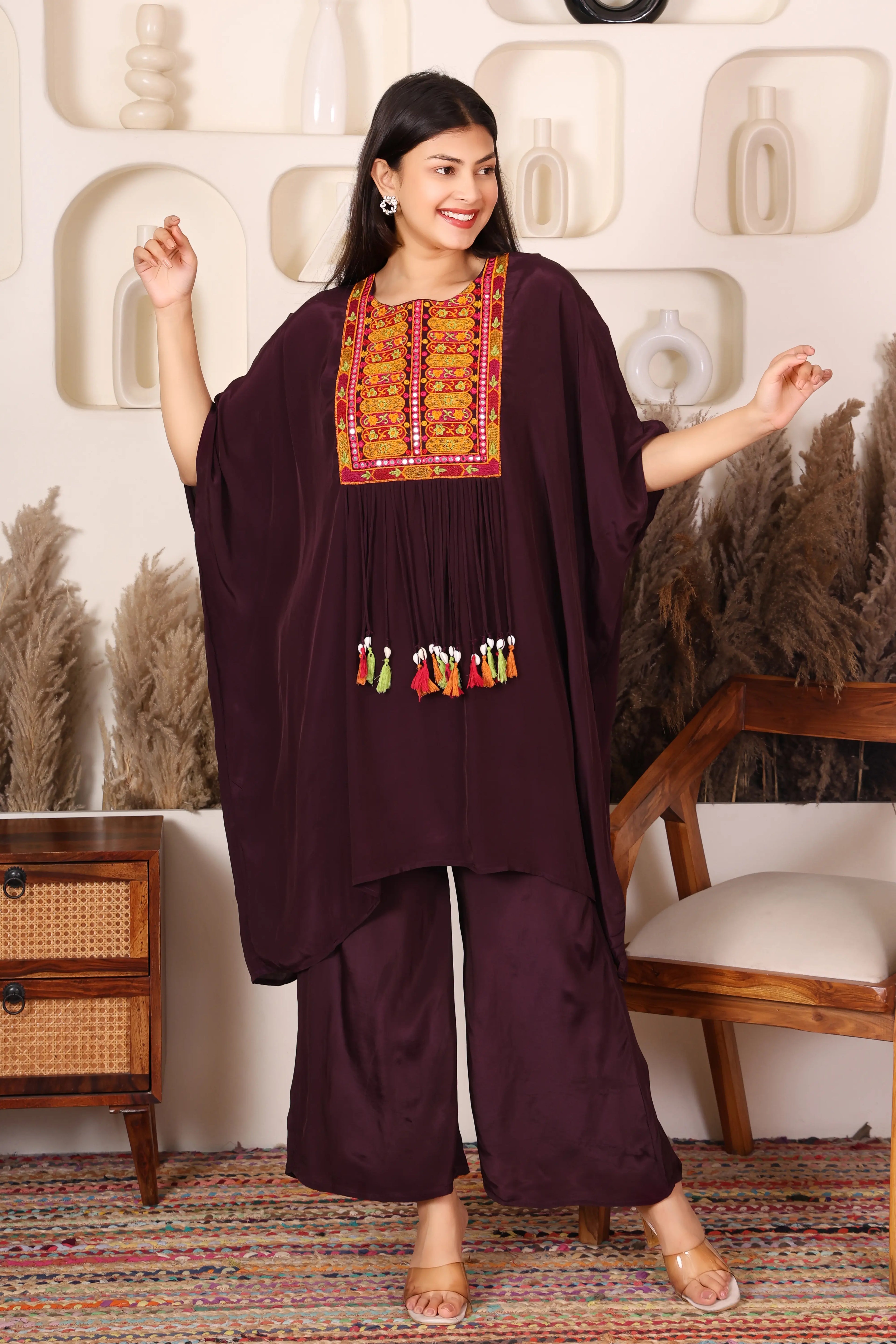 Woman wearing a dark purple traditional outfit with colorful embroidery in a decorative setting.