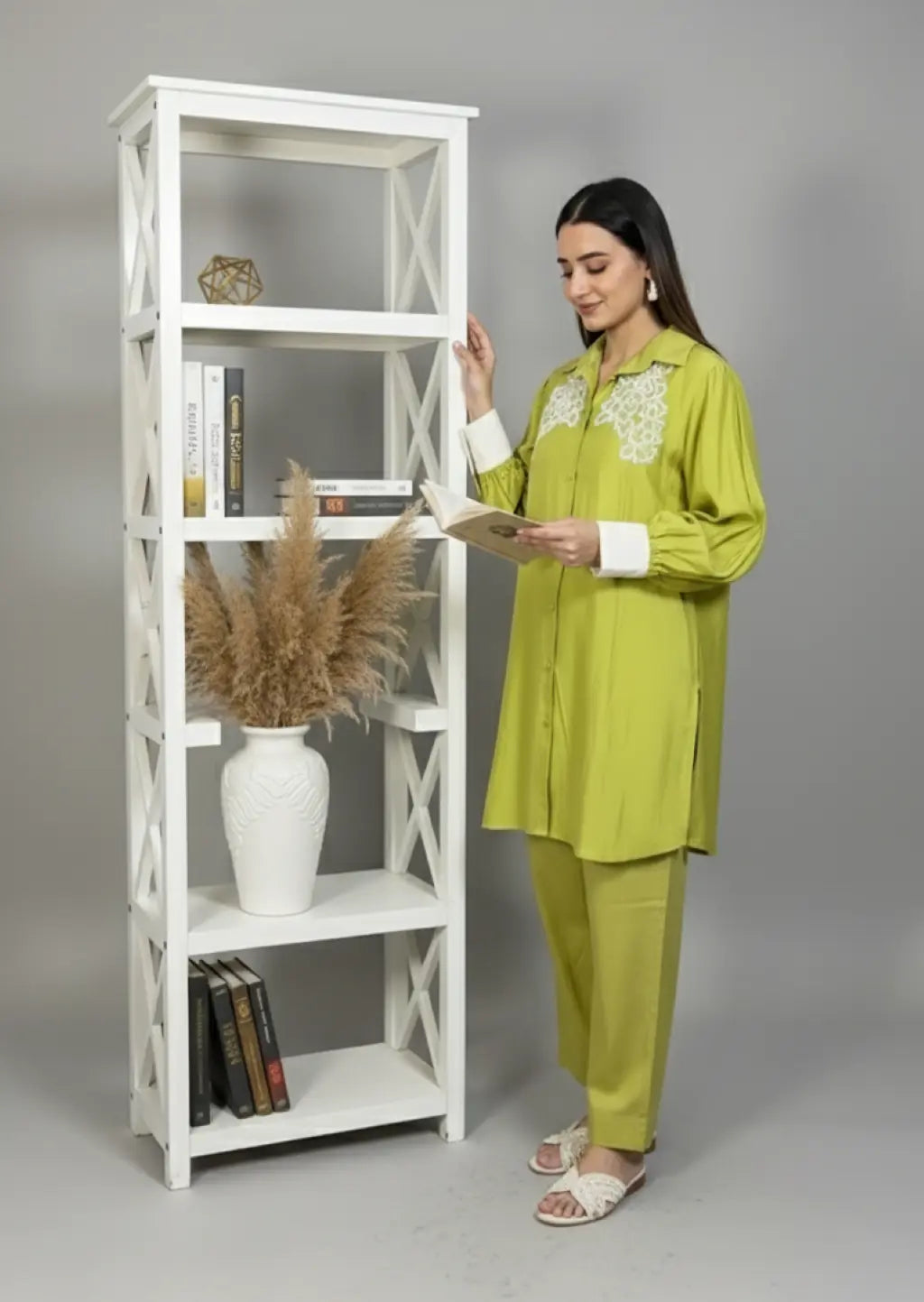 Woman in a green outfit standing next to a white bookshelf.