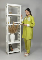 Woman in a green outfit standing next to a white bookshelf.