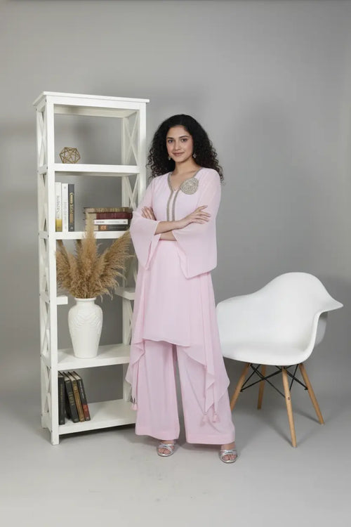 Woman wearing A soft pink pure georgette kurti set featuring fine cutdana and stone work, paired with crepe bell-bottom pants.