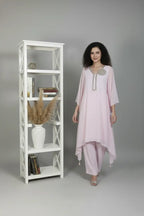 Woman wearing A soft pink pure georgette kurti set featuring fine cutdana and stone work, paired with crepe bell-bottom pants.