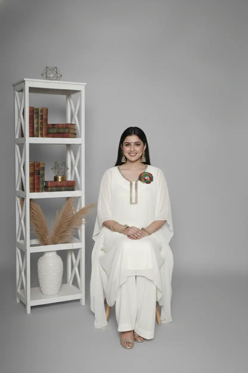 Woman wearing ivory Reagan-style kaftan co-ord set, crafted in pure georgette with vibrant thread floral applique and delicate cutdana accents. Paired with crepe bell-bottom pants and soft shantoon lining for a luxurious festive look.