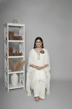 Woman wearing ivory Reagan-style kaftan co-ord set, crafted in pure georgette with vibrant thread floral applique and delicate cutdana accents. Paired with crepe bell-bottom pants and soft shantoon lining for a luxurious festive look.