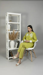 Woman in a green outfit sitting on a white chair next to a white bookshelf against a gray background