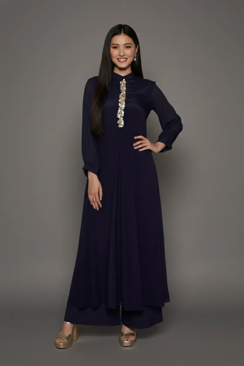 Woman wearing a sophisticated navy blue chinnon chiffon co-ord set featuring a shirt-style kurti with elegant box pleats and hand-crafted zardozi embroidery adorned with pearls and sequins. Paired with soft crepe bell-bottom pants and shantoon lining,