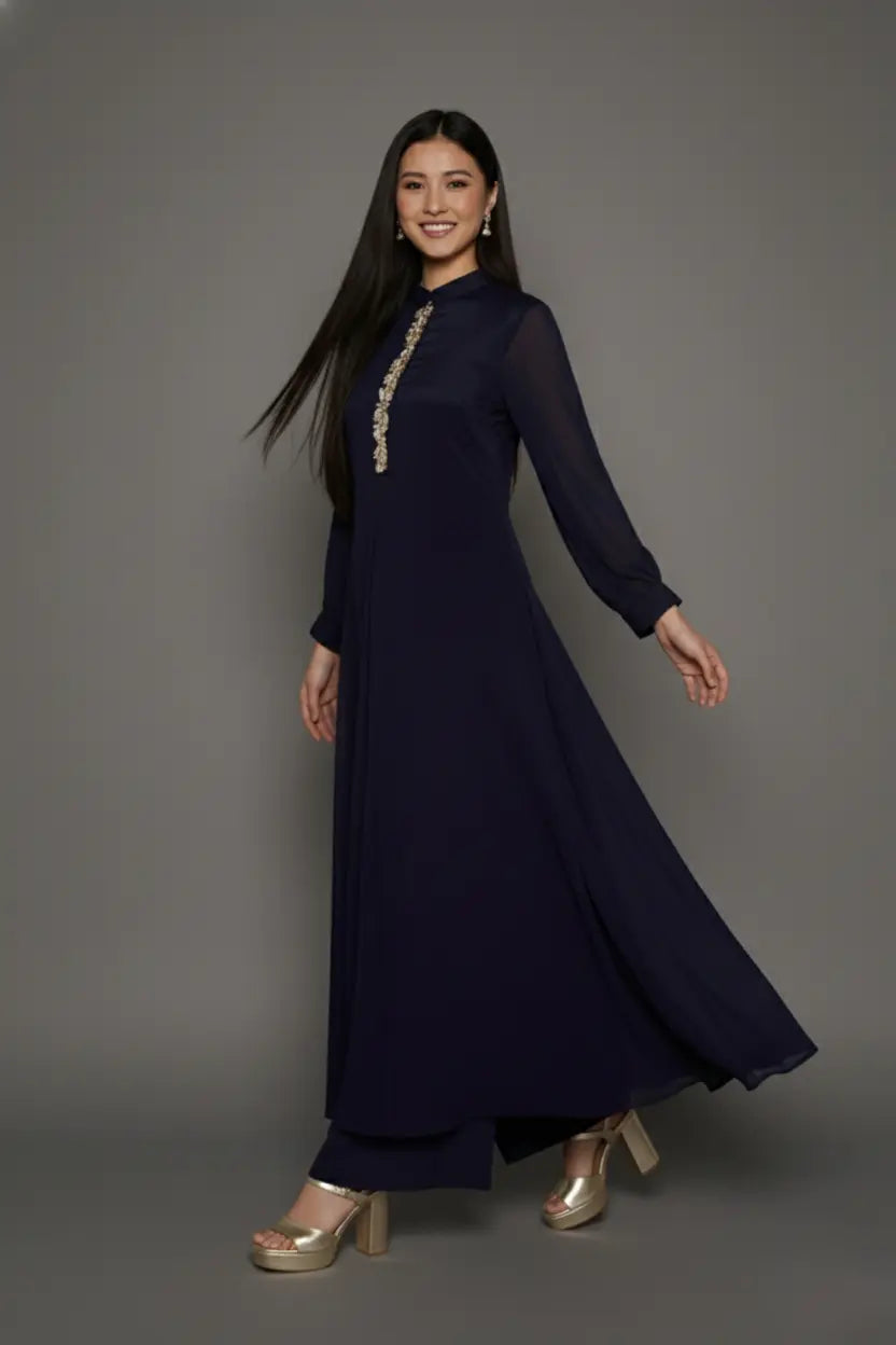Woman wearing a sophisticated navy blue chinnon chiffon co-ord set featuring a shirt-style kurti with elegant box pleats and hand-crafted zardozi embroidery adorned with pearls and sequins. Paired with soft crepe bell-bottom pants and shantoon lining,