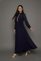 Woman wearing a sophisticated navy blue chinnon chiffon co-ord set featuring a shirt-style kurti with elegant box pleats and hand-crafted zardozi embroidery adorned with pearls and sequins. Paired with soft crepe bell-bottom pants and shantoon lining,