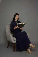 Woman wearing a sophisticated navy blue chinnon chiffon co-ord set featuring a shirt-style kurti with elegant box pleats and hand-crafted zardozi embroidery adorned with pearls and sequins. Paired with soft crepe bell-bottom pants and shantoon lining,