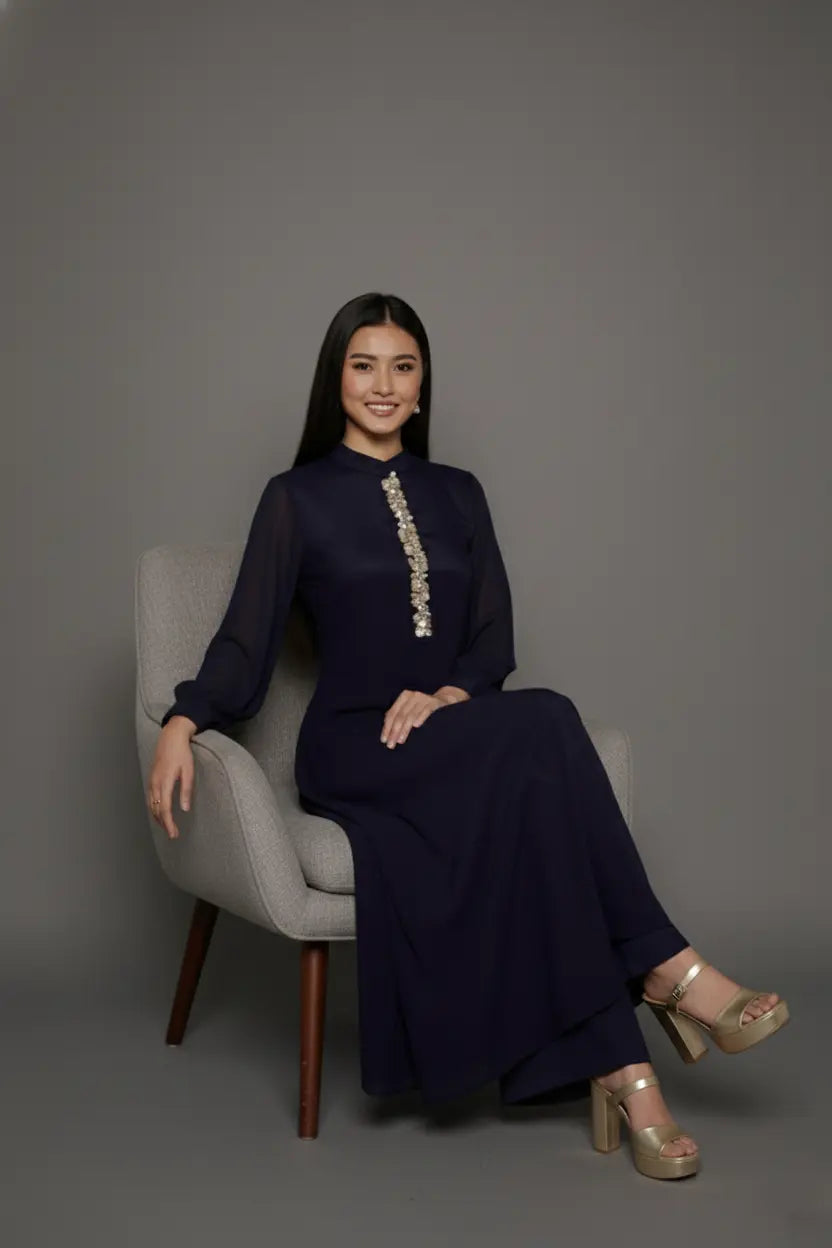 Woman wearing a sophisticated navy blue chinnon chiffon co-ord set featuring a shirt-style kurti with elegant box pleats and hand-crafted zardozi embroidery adorned with pearls and sequins. Paired with soft crepe bell-bottom pants and shantoon lining,